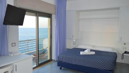 a bedroom with a bed and a balcony with the ocean at Capo Nettuno Hotel in Capo dʼOrlando