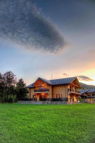 a large wooden house with a green field in front of it at Casa Pădurarului in Câmpulung Moldovenesc