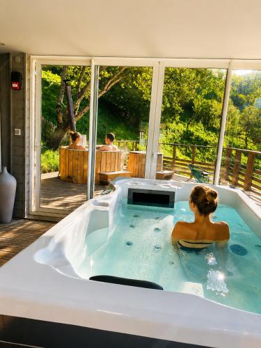 a woman sitting in a hot tub in front of a window at Solayan Nature & Spa, Piscine Intérieure, Bains Nordiques & Vue Pyrénées in Couledoux