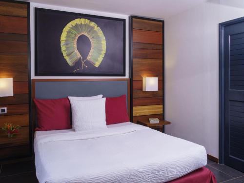 a bedroom with a large white bed with red pillows at Hotel Mercure Kourou Ariatel in Kourou