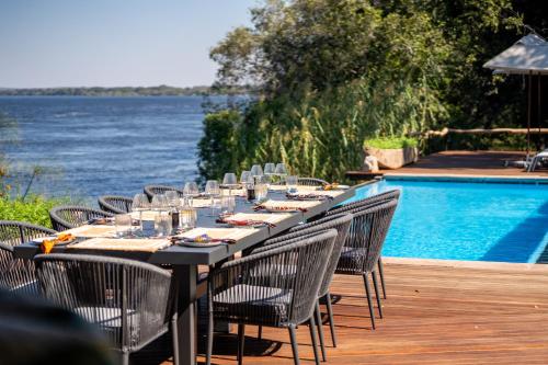 a long table with chairs next to a swimming pool at Mukwa River Lodge in Livingstone