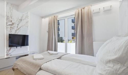 a white bedroom with a bed and a television at Ceglana Apart 01A in Katowice