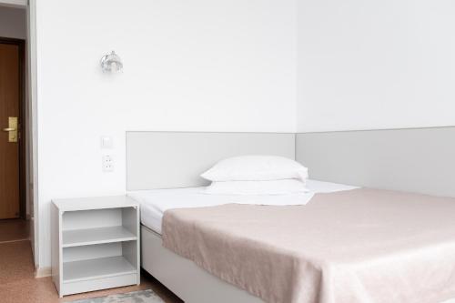 a white bedroom with a bed and a night stand at Aktobe Hotel in Aktobe