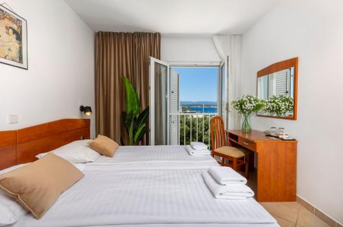 a bedroom with two beds and a desk and a window at Hotel Adria in Malinska