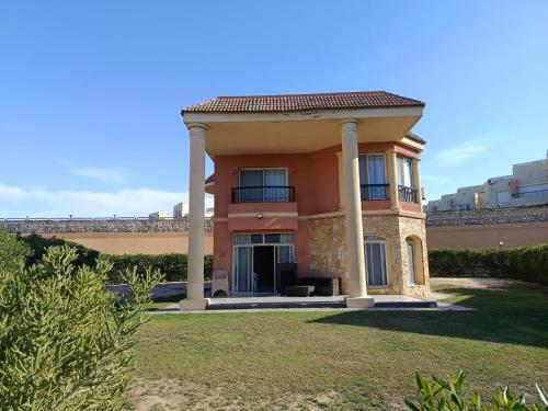 a large orange house with columns in a yard at Stand alone Villa at Blumar North coast -SIDI ABD ALRAHMAN in El Alamein