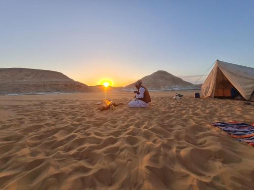a woman sitting around a fire on a beach at sunset at White Desert Experience in Bawati