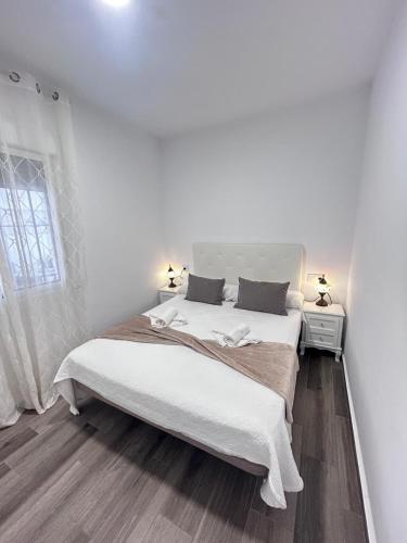 a white bedroom with a large bed and a window at Apartamento Empul Barrosa Beach in Novo Sancti Petri