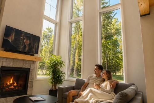 a man and woman sitting on a couch in front of a fireplace at Spa & Lake - Orphee in Chertsey