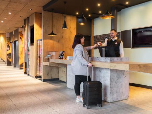 a man and a woman standing at a counter at ibis Genève Aéroport in Geneva