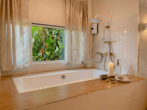 a bathroom with a bath tub with a window and a candle at Thara Coco Villa - Boutique Luxury In Srithanu in Hinkong
