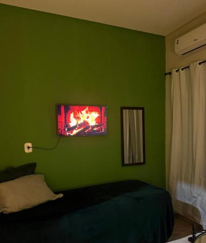 a green room with a bed and a tv on the wall at Apartamento próximo ao centro in Primavera do Leste
