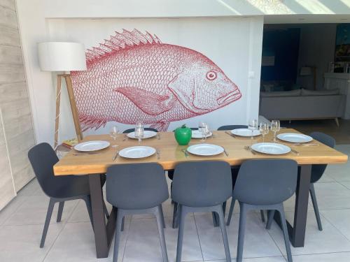 a wooden table with chairs and a fish painting on the wall at l'Herbo' MAGNIFIQUE maison à 2 pas du port de Pêche in LʼHerbaudière