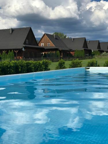 a large blue swimming pool with houses in the background at Víkendové Chalupy in Liptovský Trnovec