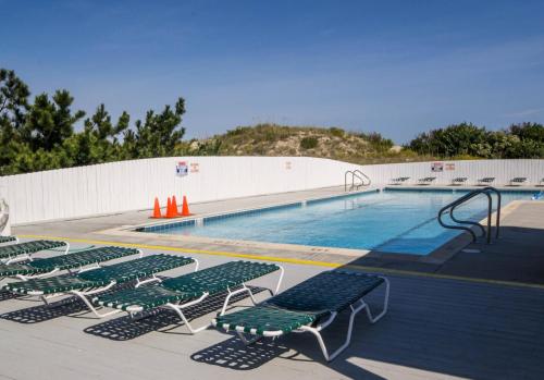 a swimming pool with green lounge chairs next to it at Into the Sun - Corolla, Villages at Ocean Hill, 75 Yds to Beach, Hot Tub, Community Pool, Pets OK, Flex Stays in Corolla