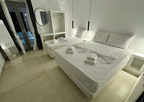 a white bedroom with two beds and a mirror at AiΘeria Suites Ios in Ios Chora