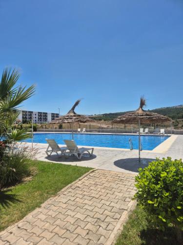 a swimming pool with two chairs and umbrellas at Marina smir Oceanica Apartments in Marina Smir