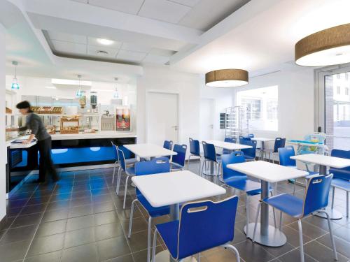 a dining room with blue chairs and tables and a person at ibis budget Torun in Toruń