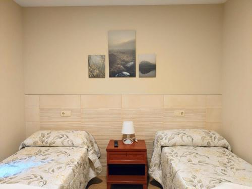 ein Schlafzimmer mit zwei Betten und einem Tisch mit Lampe in der Unterkunft ALBOR II in Gijón
