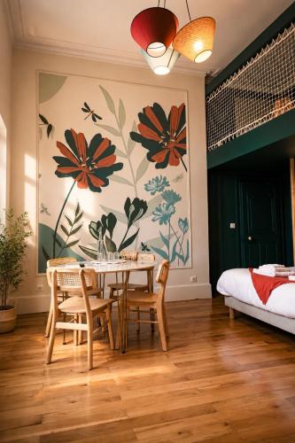 a dining room with a table and chairs and a wall with flowers at La Parenthèse Fléchoise, Chambre Raphaël in La Flèche