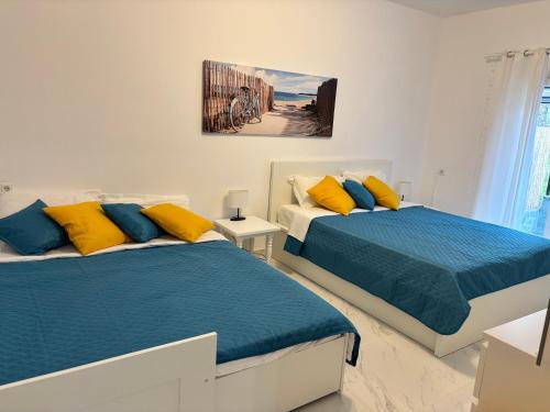 two beds in a white room with blue and yellow pillows at Vila Amore in Asprovalta