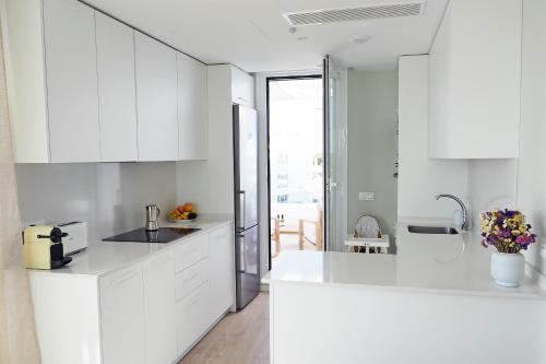 a white kitchen with white cabinets and a refrigerator at Penthouse duplex with jacuzzi, 5 min to beach in Chipiona