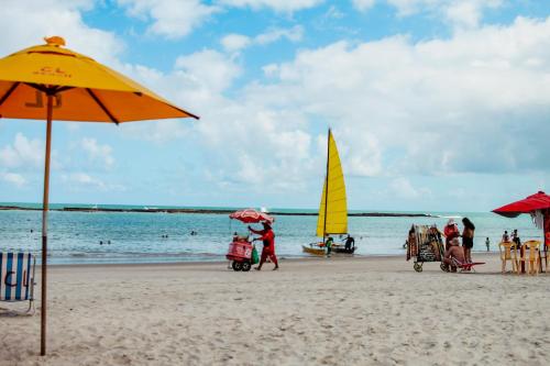 a beach with a yellow umbrella and a sail boat at Praia do Frances - Casa Vista para o Mar - 50 metros da areia da praia in Praia do Frances