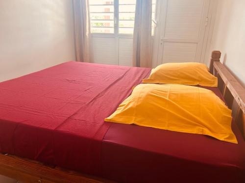 a bed with red and yellow sheets and a window at Cap Alizés in Petit-Canal