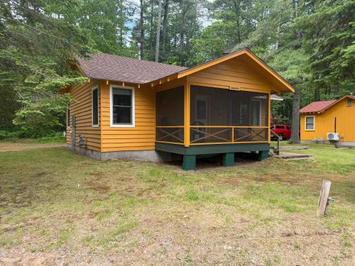 a small yellow house with a porch in a yard at Chickadee Cabin in Saint Germain