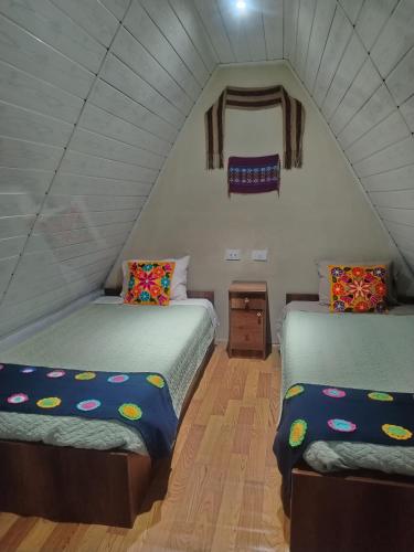 two twin beds in a room with a attic at Hay & Mountain Huts in Colcapampa