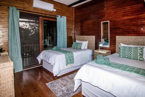 two beds in a room with wooden walls and windows at 56 Crocodile in Komatipoort