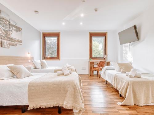 two beds in a room with white walls and wooden floors at Aida's Hostal in Puentes de García Rodríguez