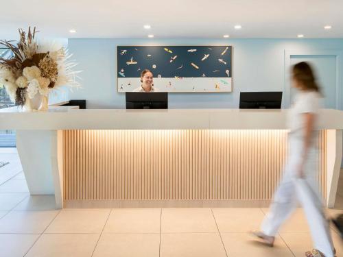 a woman walking past a reception desk in a lobby at The Sebel Kiama in Kiama