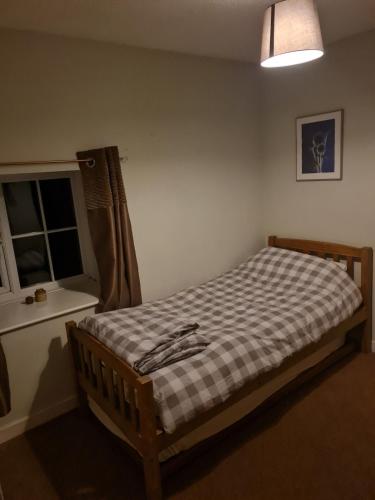 a bedroom with a bed with a checkered blanket and a window at Bwthyn canol in Sennybridge