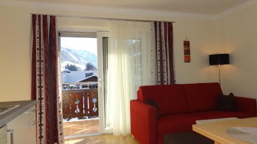 ein Wohnzimmer mit einer roten Couch und einer Glasschiebetür in der Unterkunft Appartements Gassner in Bruck an der Großglocknerstraße