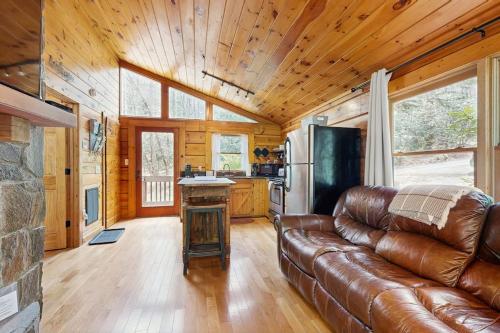 a living room with a leather couch and a kitchen at Creeksong Cabin in Topton