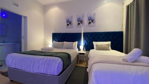 two beds in a hotel room with purple lighting at The Oasis Guesthouse in Mtubatuba