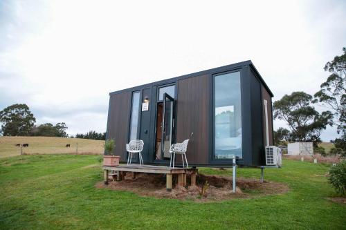 a black tiny house with two chairs and a bench at Bayview Paradise by Tiny Away in Diamond Harbour