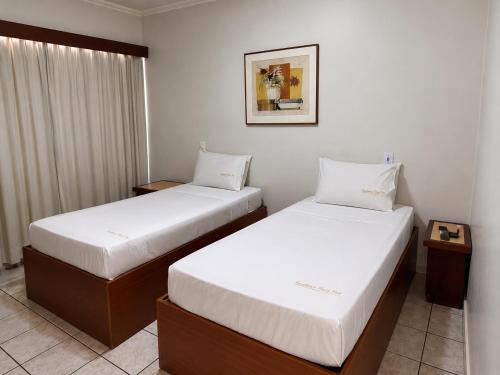 two beds in a hotel room with white sheets at Flat Vintage in Ribeirão Preto
