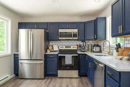 a kitchen with blue cabinets and a stainless steel refrigerator at Tucked in the Woods - Jacuzzi Firepit Pooltable in Long Pond