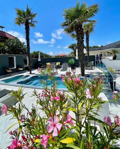 a patio with palm trees and a swimming pool with pink flowers at AGATA BEACH Boutique -Adult Only in Ahtopol