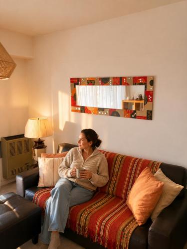a woman sitting on a couch in a living room at CASA MENDIOLA, encantadora casa con patio privado, y pileta en jardín cerca de la Laguna in Chascomús