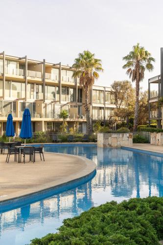 a hotel with a swimming pool with tables and blue umbrellas at Wyndham Resort Torquay in Torquay