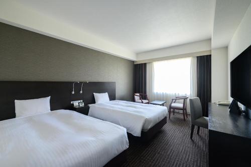 a hotel room with two beds and a desk at KKR Hotel Nagoya in Nagoya