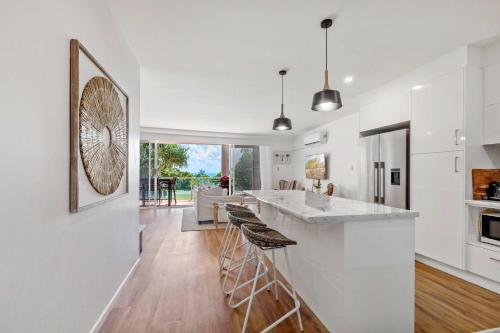 a kitchen with white walls and a large island with bar stools at Sophisticated & stylish beachside apartment with pool in Sunrise Beach