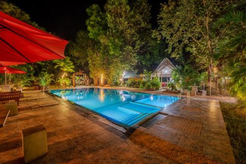 a swimming pool at night with a red umbrella at Dudley Nature Resort in Habarana