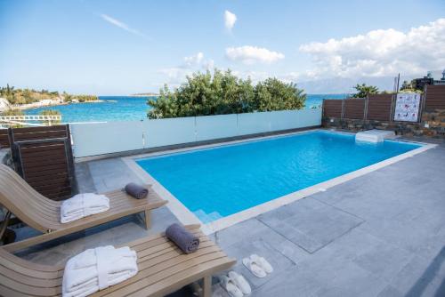 a swimming pool with two lounge chairs next to the ocean at Ammos Lux Apartments Crete in Agios Nikolaos