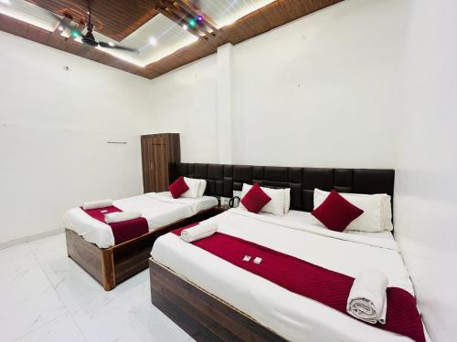 two beds in a room with white walls and red pillows at Hotel Shreeji Palace - OPP Hanuman Garhi Mandir in Ayodhya