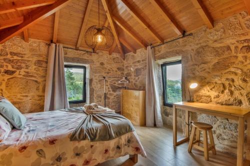 a bedroom in a stone house with a bed and a desk at Casa De Pedra D'alborinhas in Arões