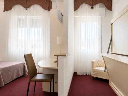 a room with a bed and a desk and two windows at Hotel Da Mario in Caorle