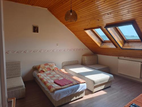 a attic room with two beds and two windows at Leveleki Eszter Üdülő in Bánk